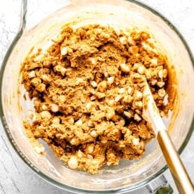 white chocolate and macadamia nuts mixed into the cookie batter in a clear stand mixer bowl with white spatula