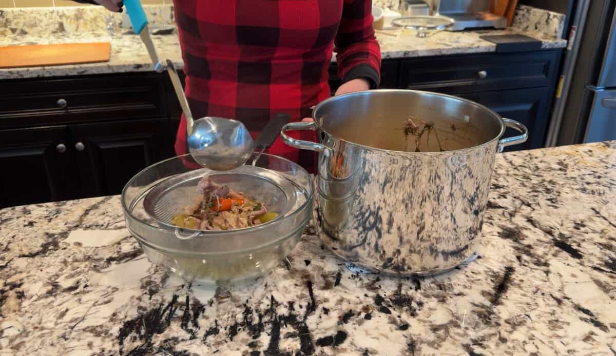 straining out the chicken stock ingredients and liquid