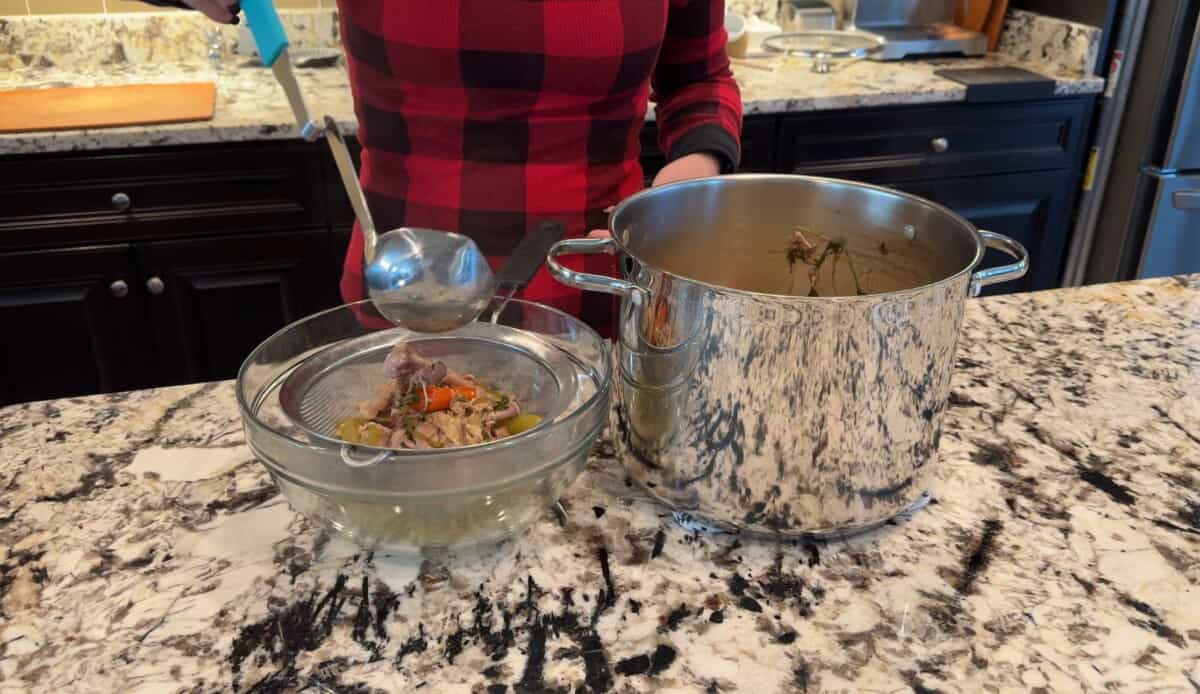 straining out the chicken stock ingredients and liquid