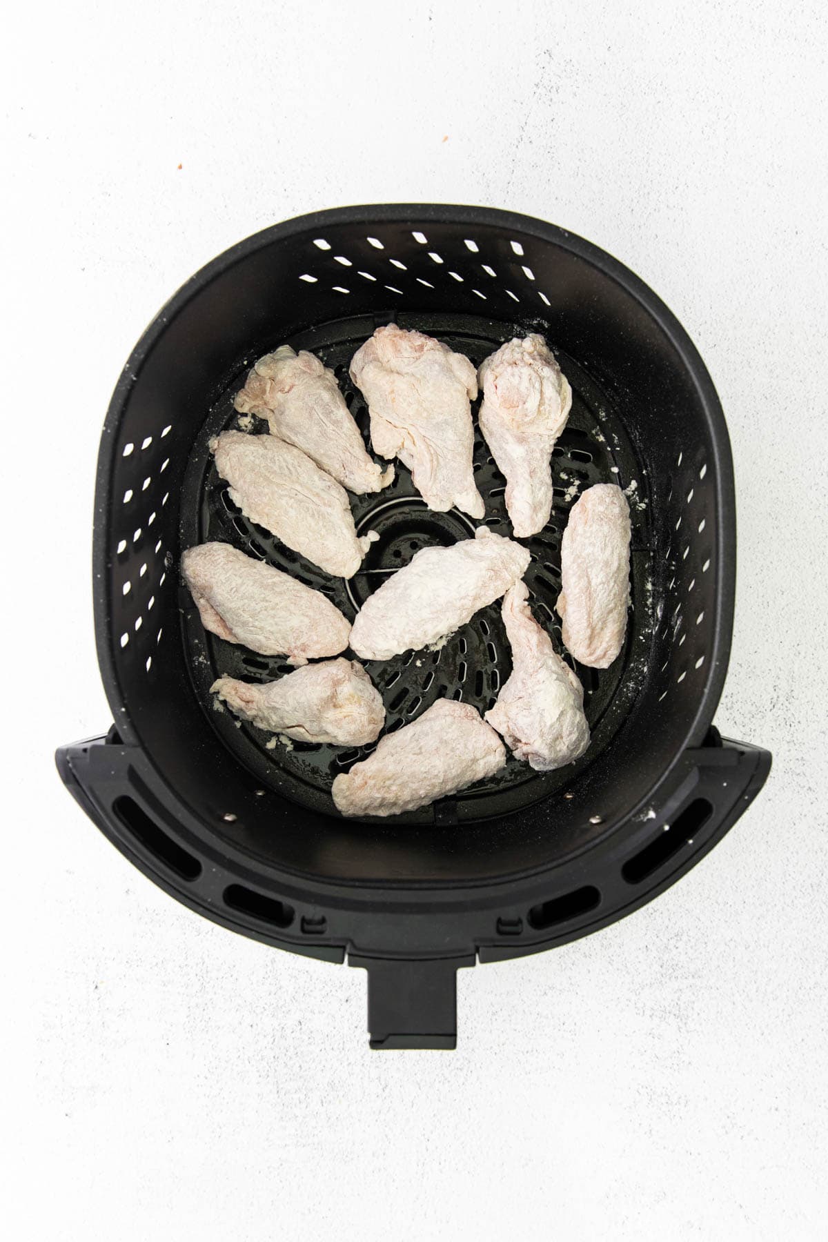 chicken wings in the basket of an air fryer tossed in flour
