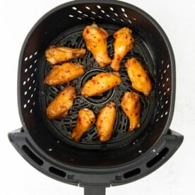 air fryer chicken wings tossed in a sweet chili sauce in the basket of an air fryer