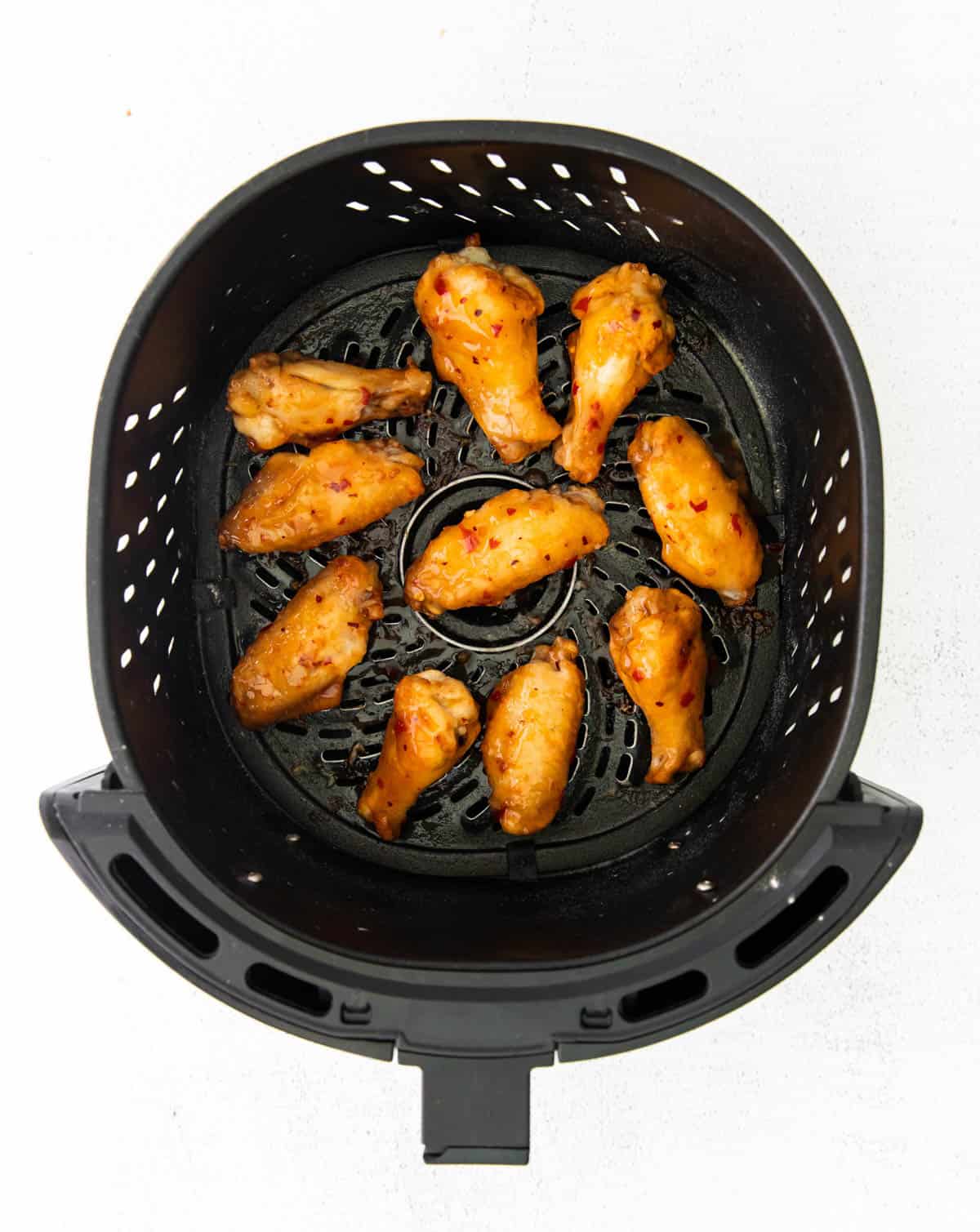 air fryer chicken wings tossed in a sweet chili sauce in the basket of an air fryer