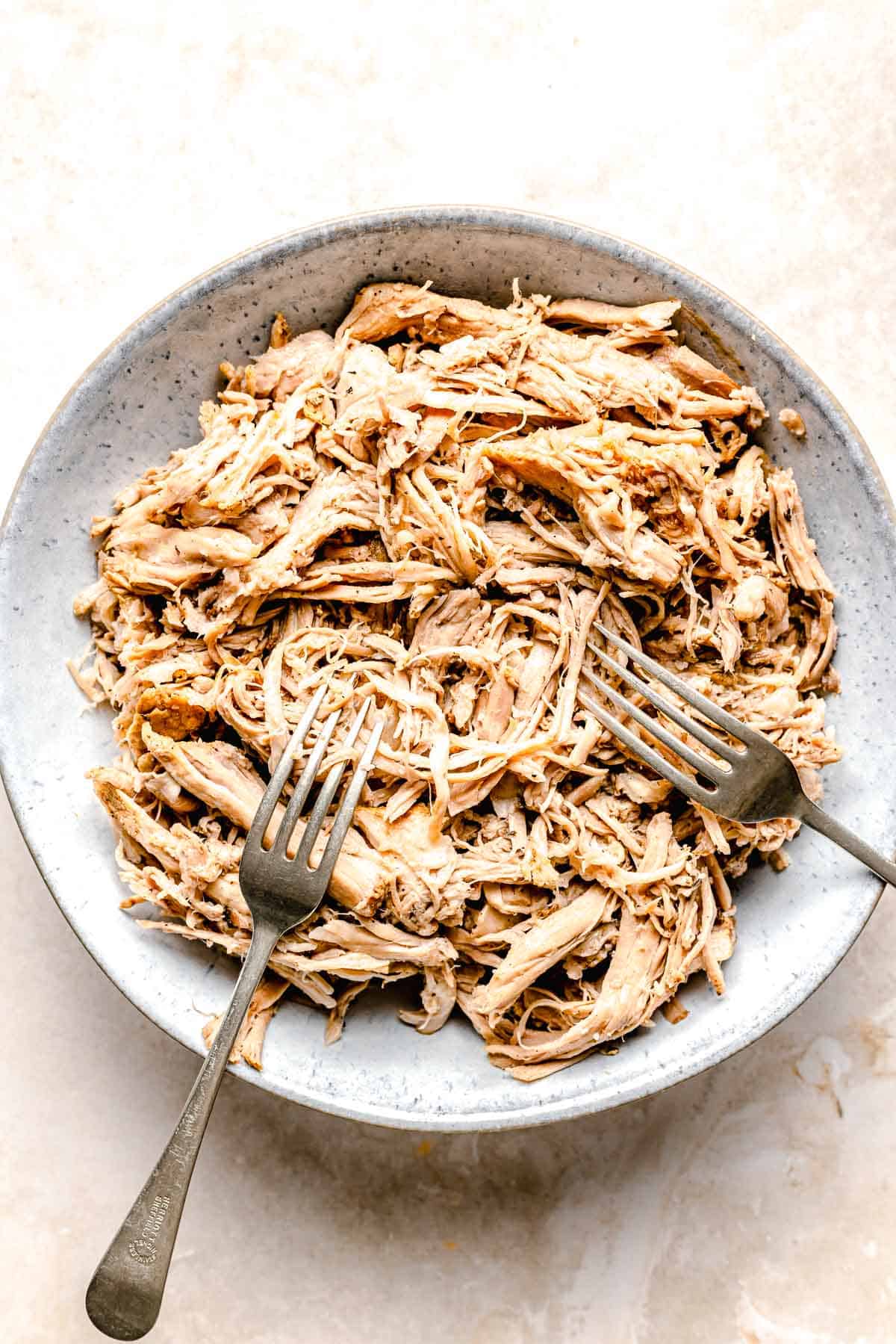 Shredding pork with two forks in a bowl.