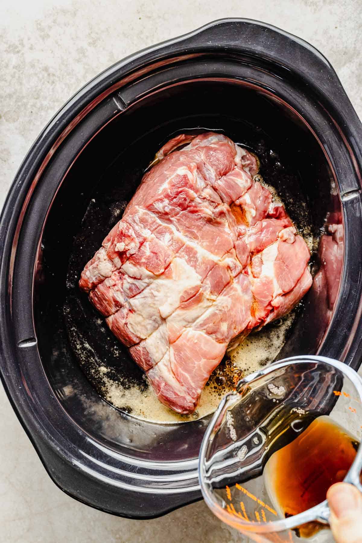 Pouring soda over pork in a crock pot.