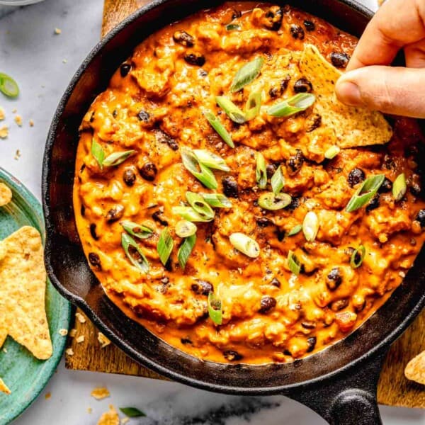 Overhead image of scooping a bite of chili cheese dip out of a skillet with a tortilla chip.