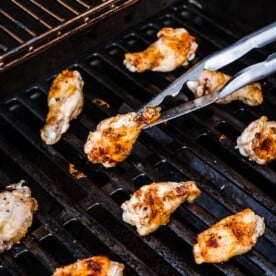 a metal tong is grasping a chicken wing on the grill