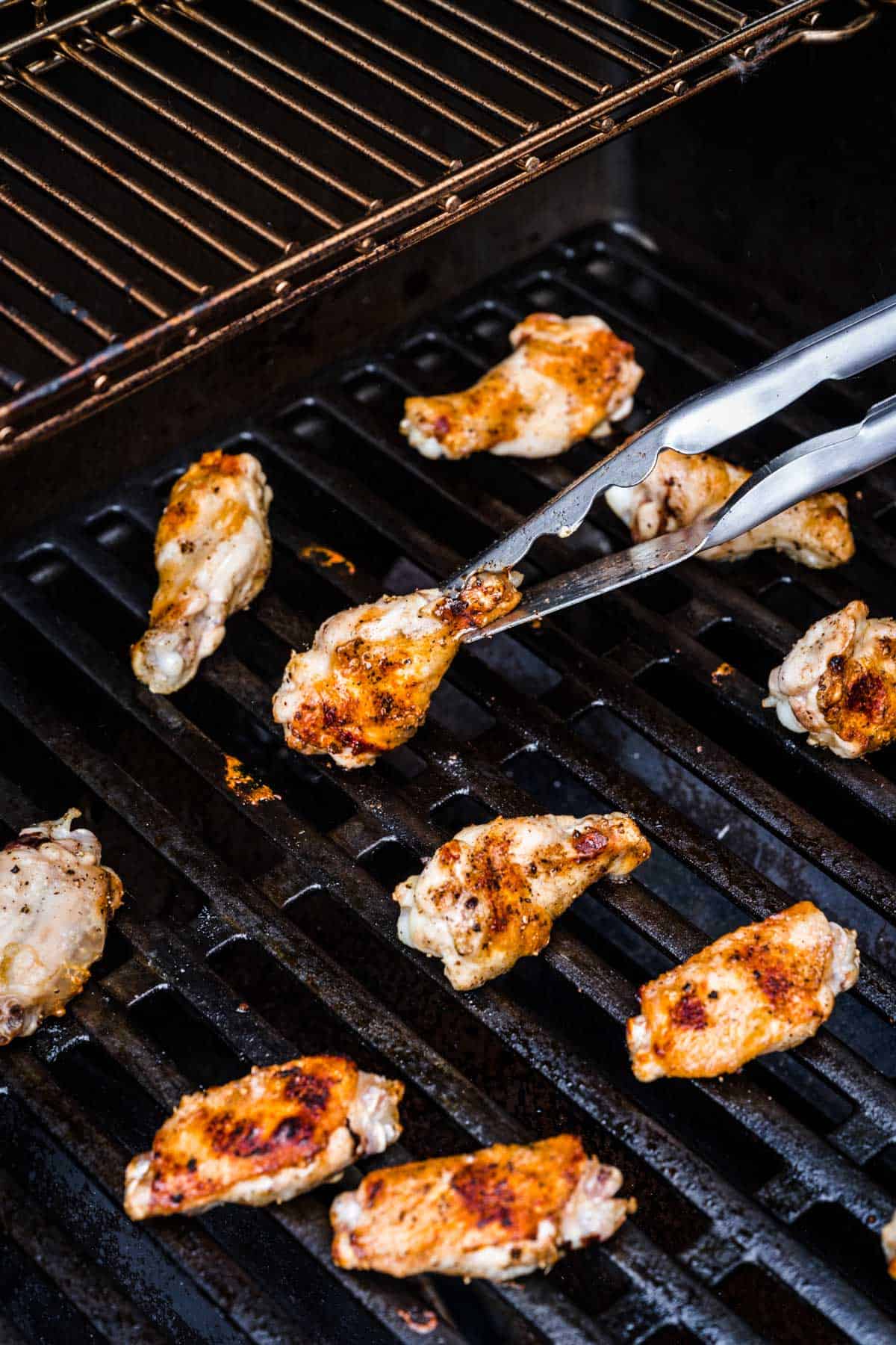 a metal tong is grasping a chicken wing on the grill