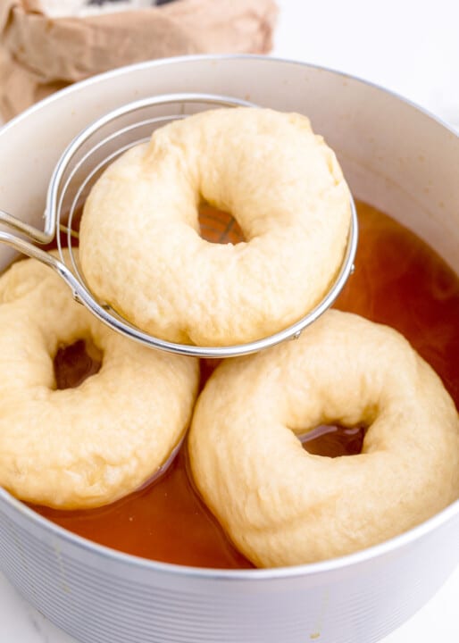 a metal slotted spoon scooping out bagel dough from the water bath