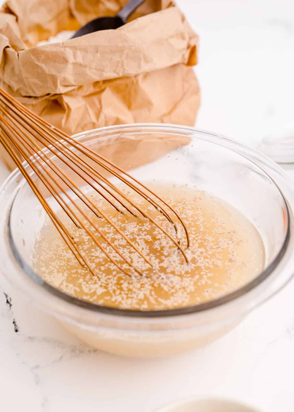 whisking together yeast, water, and maple syrup in a clear bowl