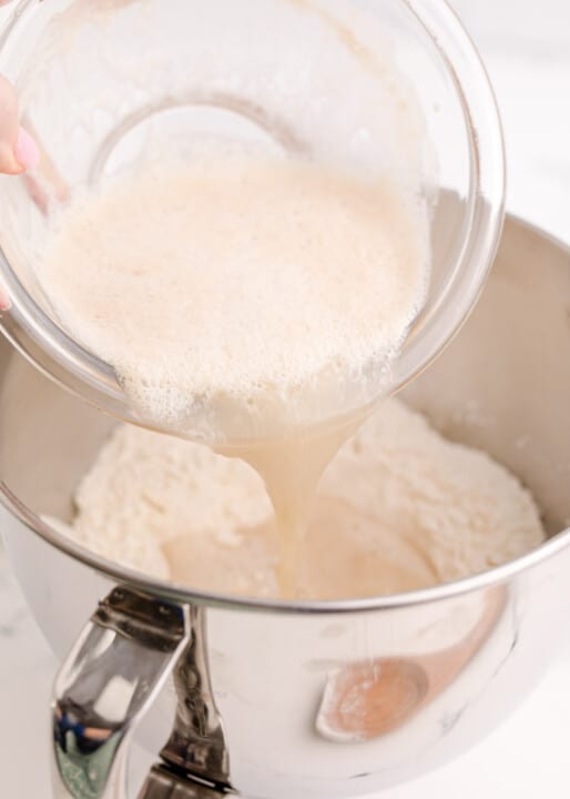 adding yeast mixture to a metal stand mixer bowl with flour