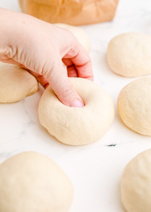 a thumb indenting the center of the dough to create the bagel hole