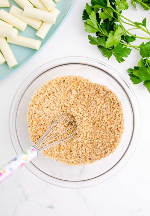 whisking breadcrumbs and panko breadcrumbs together in a clear bowl