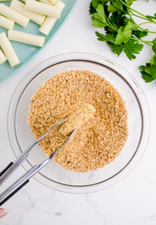 dipping the mozzarella stick into the breadcrumb mixture with a metal tong