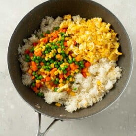rice, vegetables, and eggs added into a grey wok