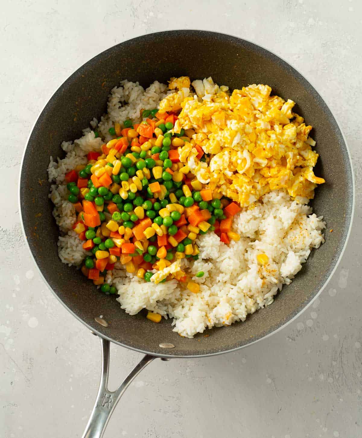 rice, vegetables, and eggs added into a grey wok