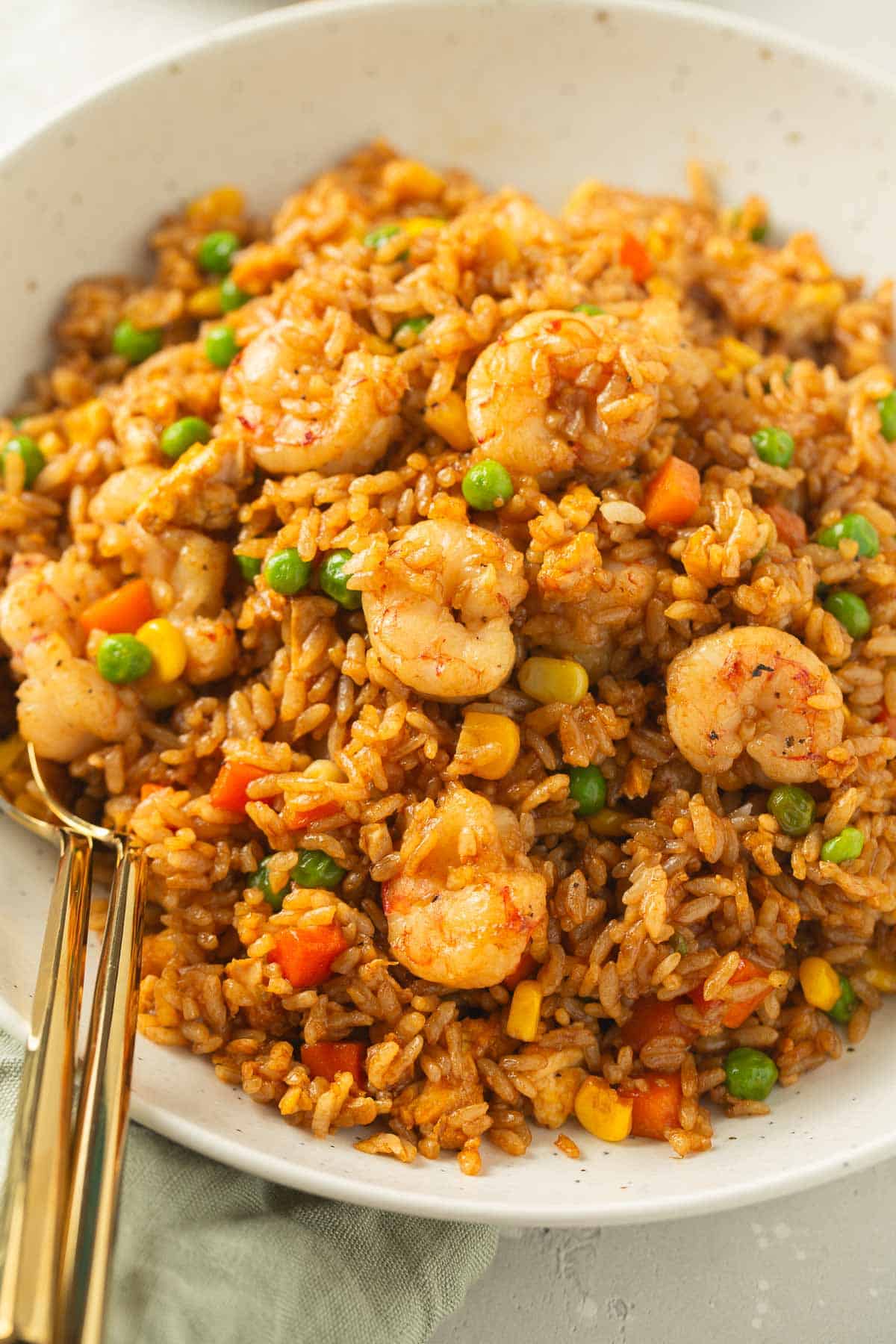 shrimp fried rice in a speckled bowl with gold metal spoons