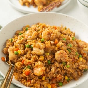 shrimp fried rice with two metal spoons in a large speckled bowl next to a green linen towel