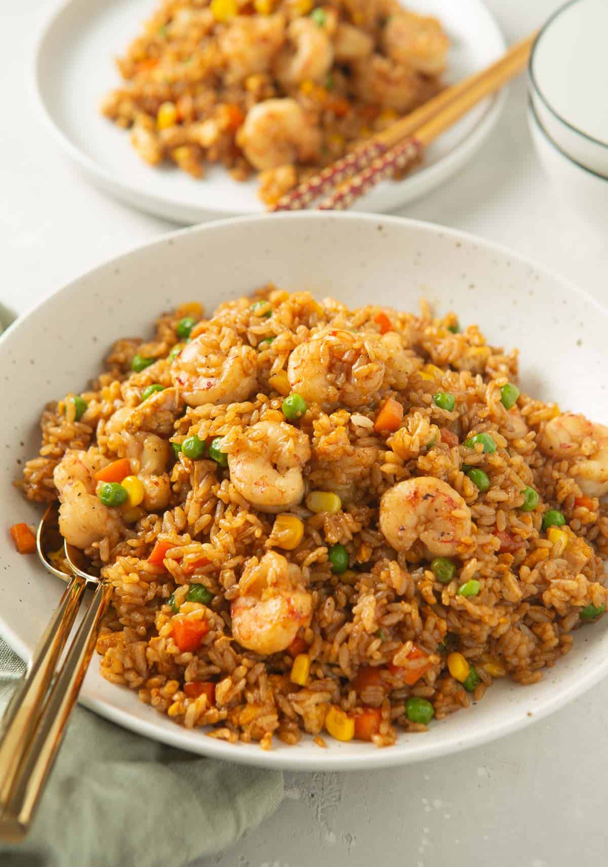 shrimp fried rice with two metal spoons in a large speckled bowl next to a green linen towel