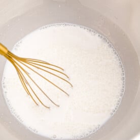 a gold whisk in a milk mixture in the bowl of a metal stand mixer