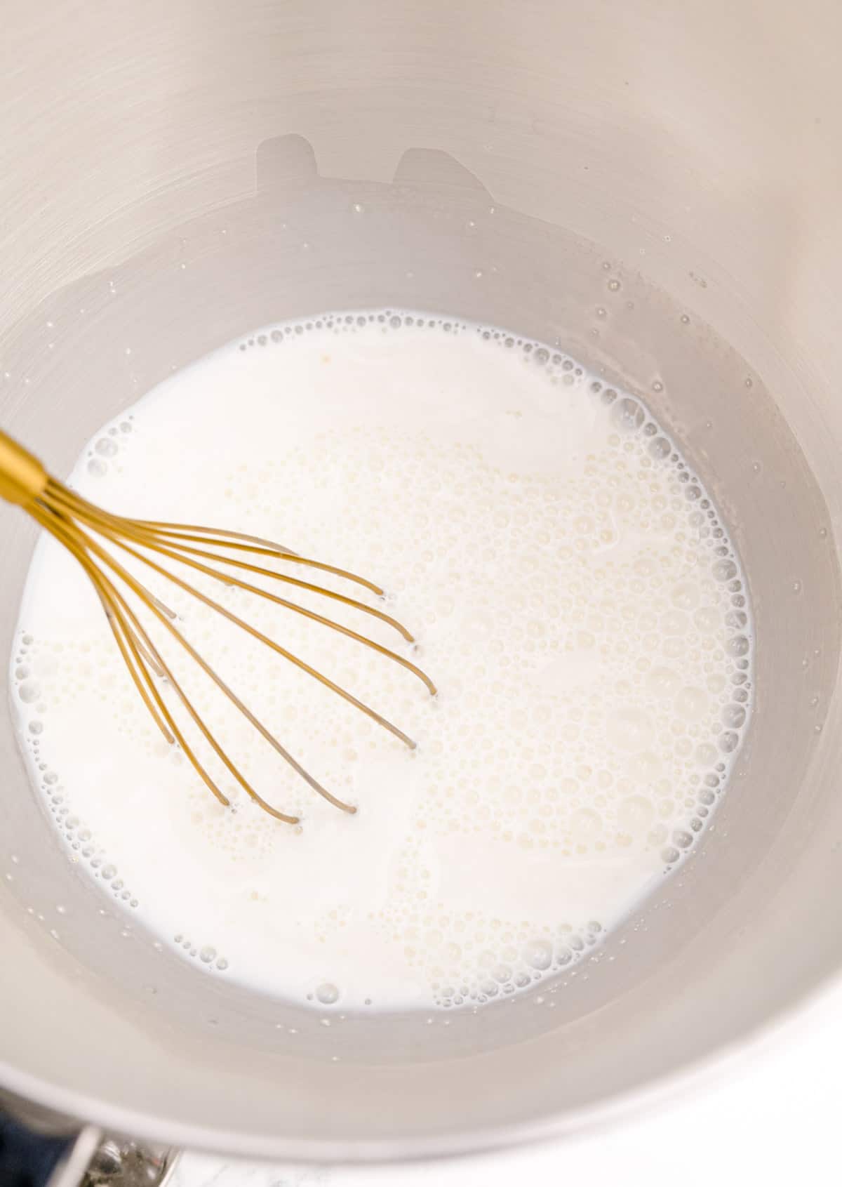a gold whisk in a milk mixture in the bowl of a metal stand mixer