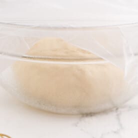 covered dough in a clear bowl rising