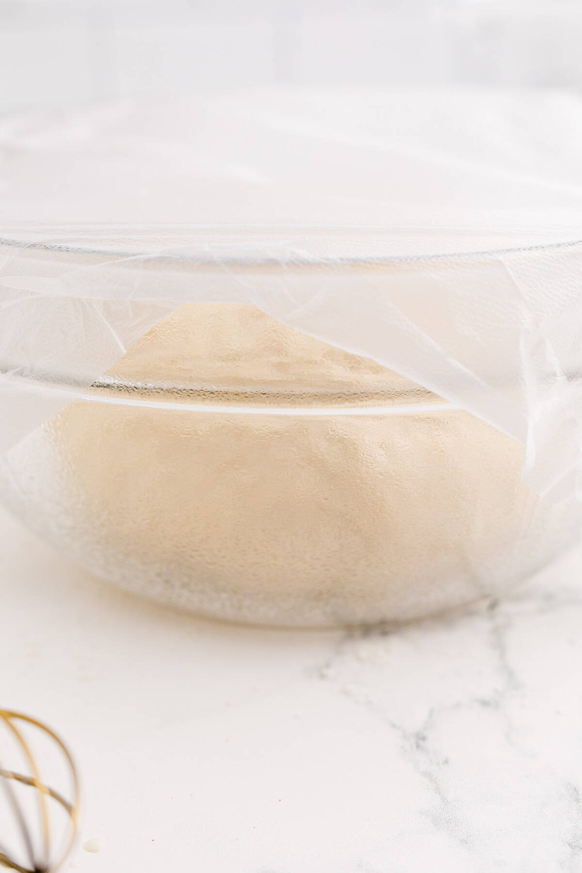 covered dough in a clear bowl rising