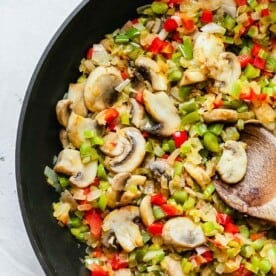 mushrooms, celery, onions, and bell peppers in a large skillet with a wooden spoon