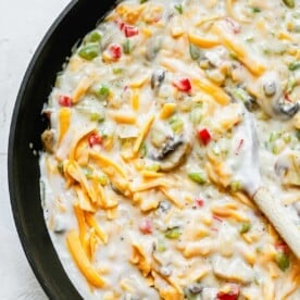 vegetable mixture with milk and cream of mushroom and shredded cheese in a skillet with a wooden spoon