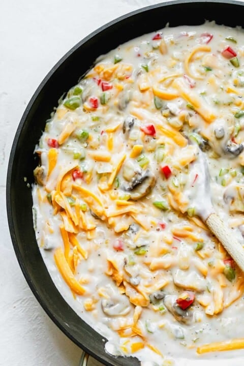 vegetable mixture with milk and cream of mushroom and shredded cheese in a skillet with a wooden spoon