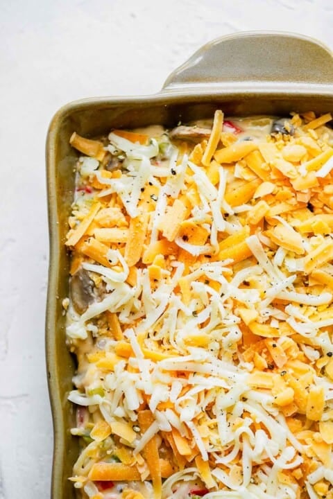 freshly shredded cheese on top of spaghetti mixture in a casserole dish