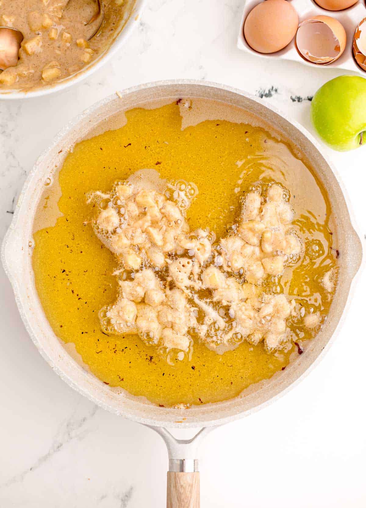 apple fritters frying in a large skillet with oil