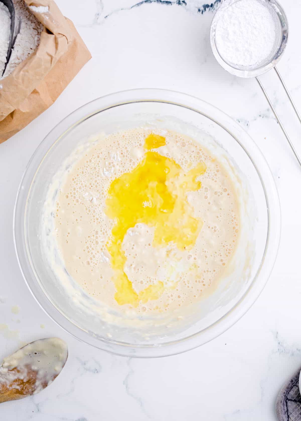 butter and egg added into a clear bowl with flour and yeast