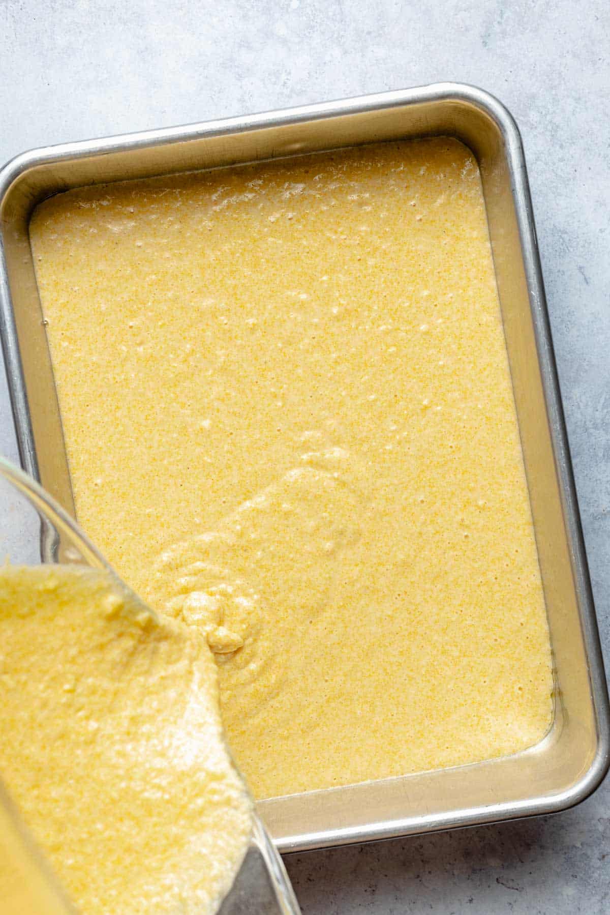 Pouring cornbread batter into a baking pan.