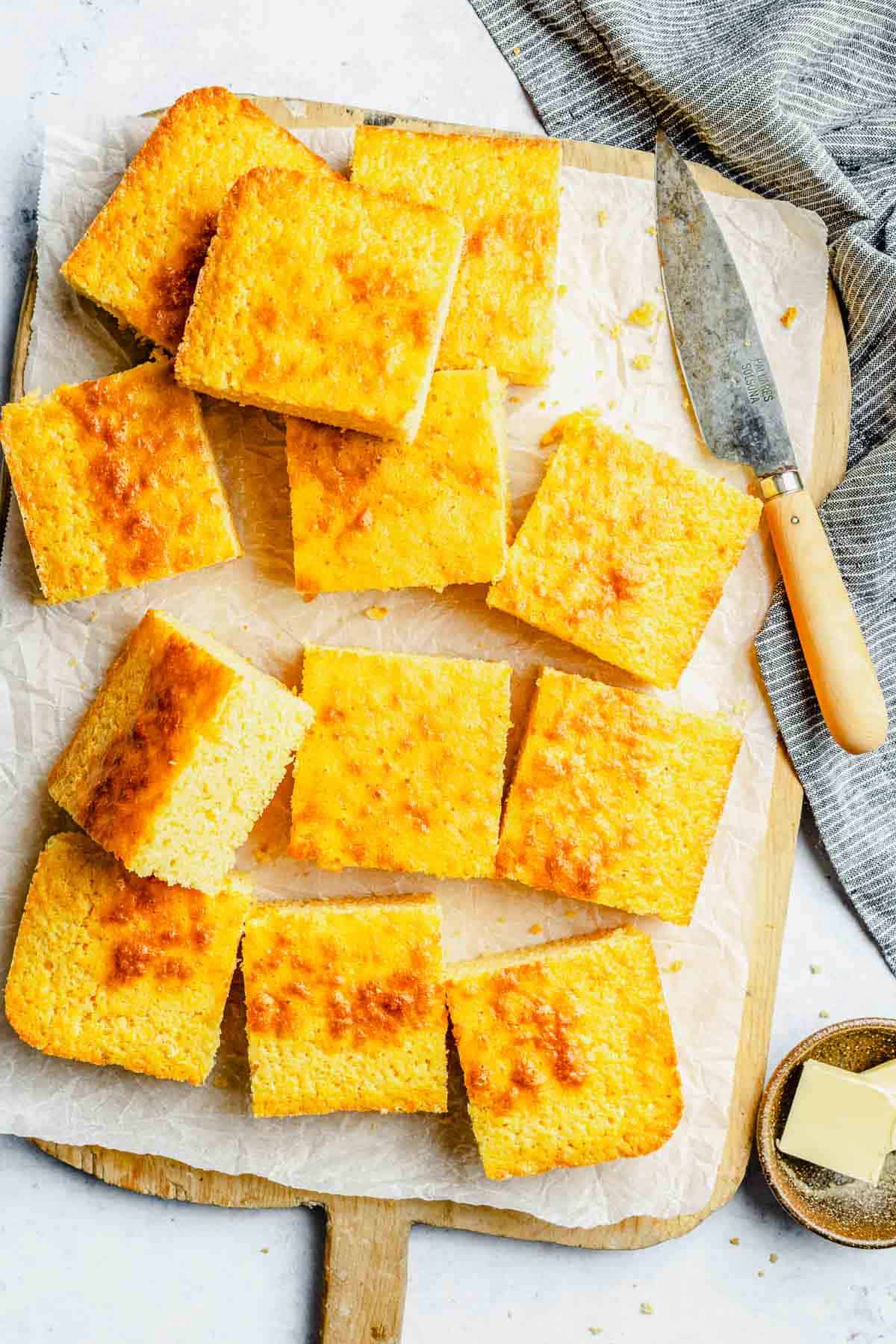 Overhead image of slices of cornbread stacked on a cutting board lined with parchment paper.