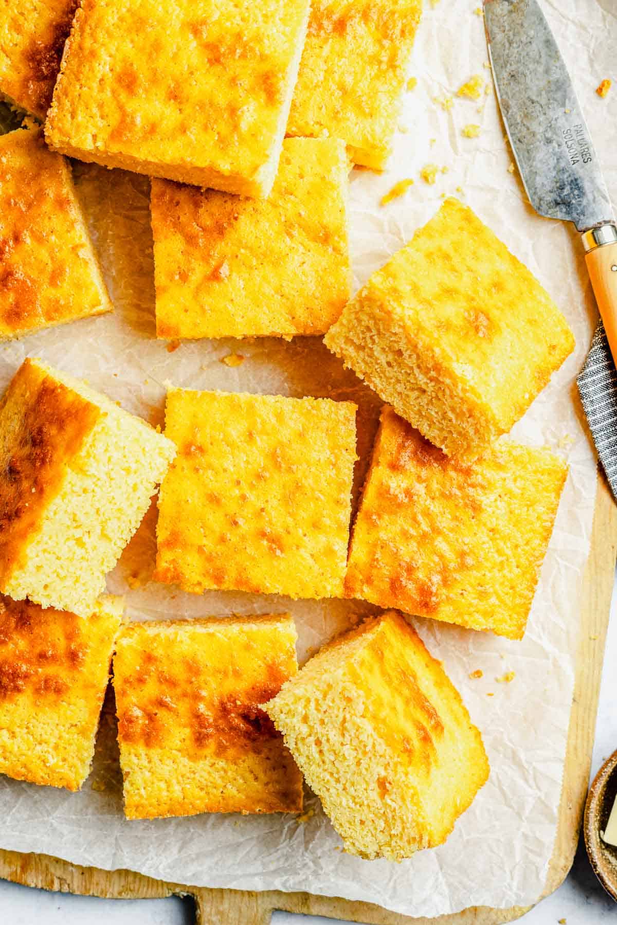 Closeup overhead image of slices of cornbread stacked on a cutting board lined with parchment paper.