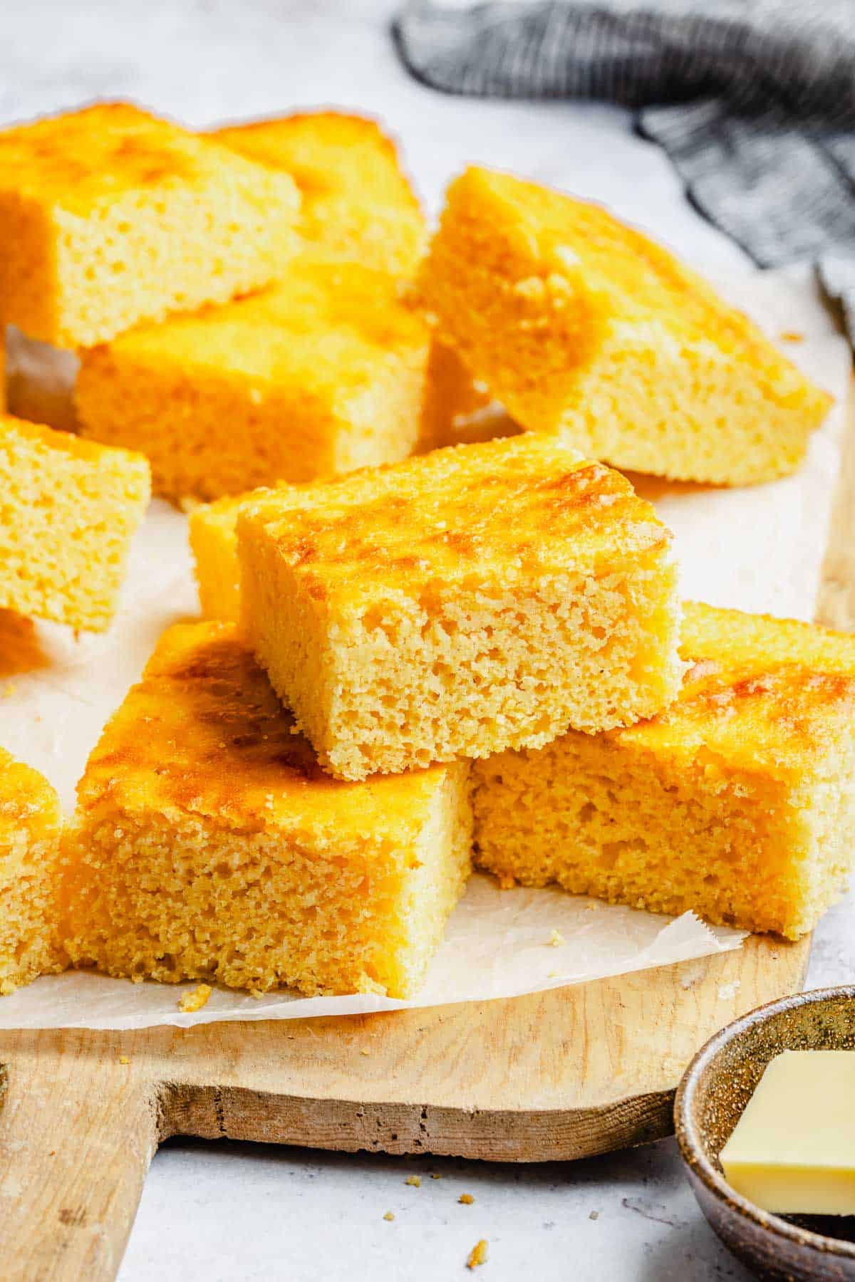 Slices of cornbread stacked on a cutting board lined with parchment paper.