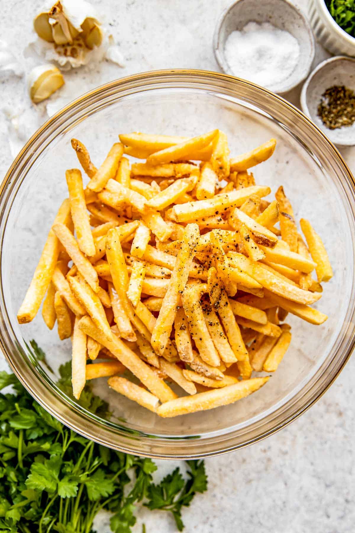 Fries are placed in a glass bowl with seasonings. 