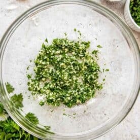 Garlic, parsley and oil are mixed together in a bowl.