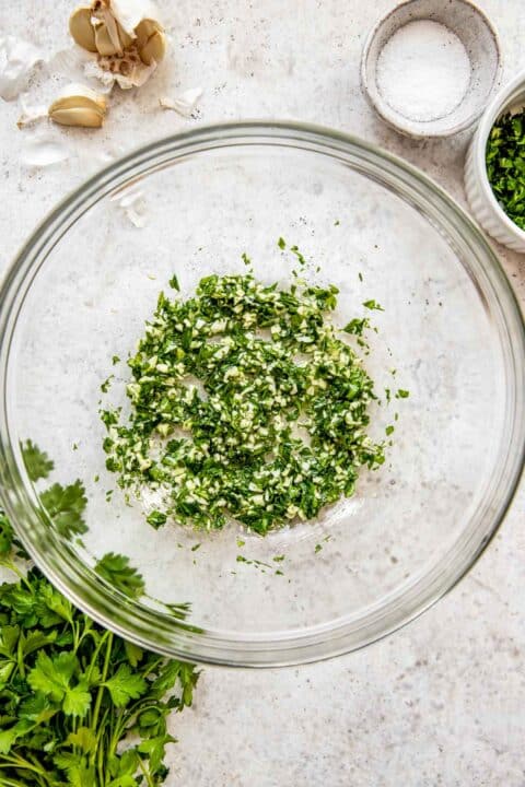 Garlic, parsley and oil are mixed together in a bowl.