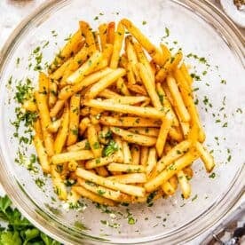 Cooked fries are tossed in a bowl with parsley and garlic.