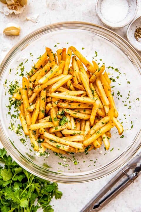 Cooked fries are tossed in a bowl with parsley and garlic.