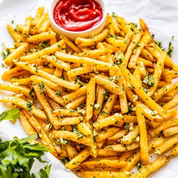 A small bowl of ketchup is placed on a tray filled with fries.