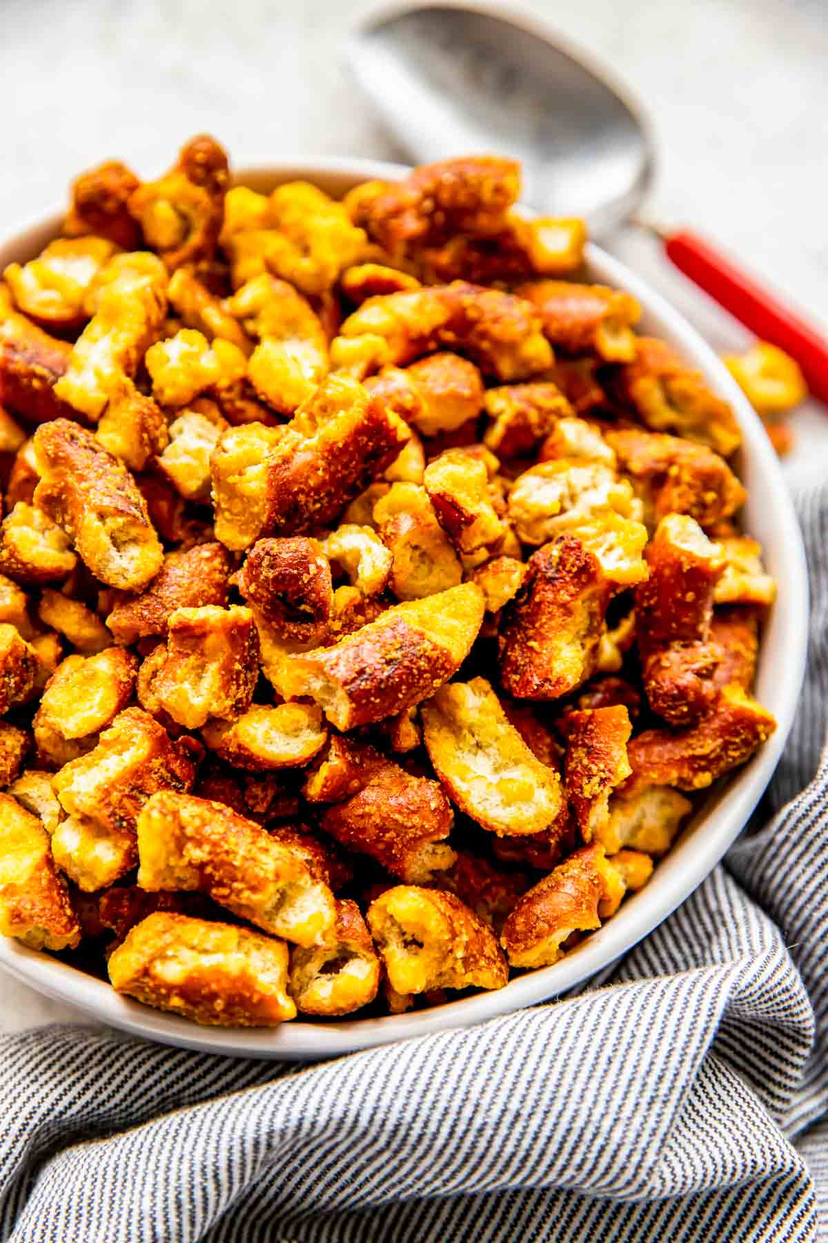 A scoop is placed next to a full bowl of honey mustard pretzels. 