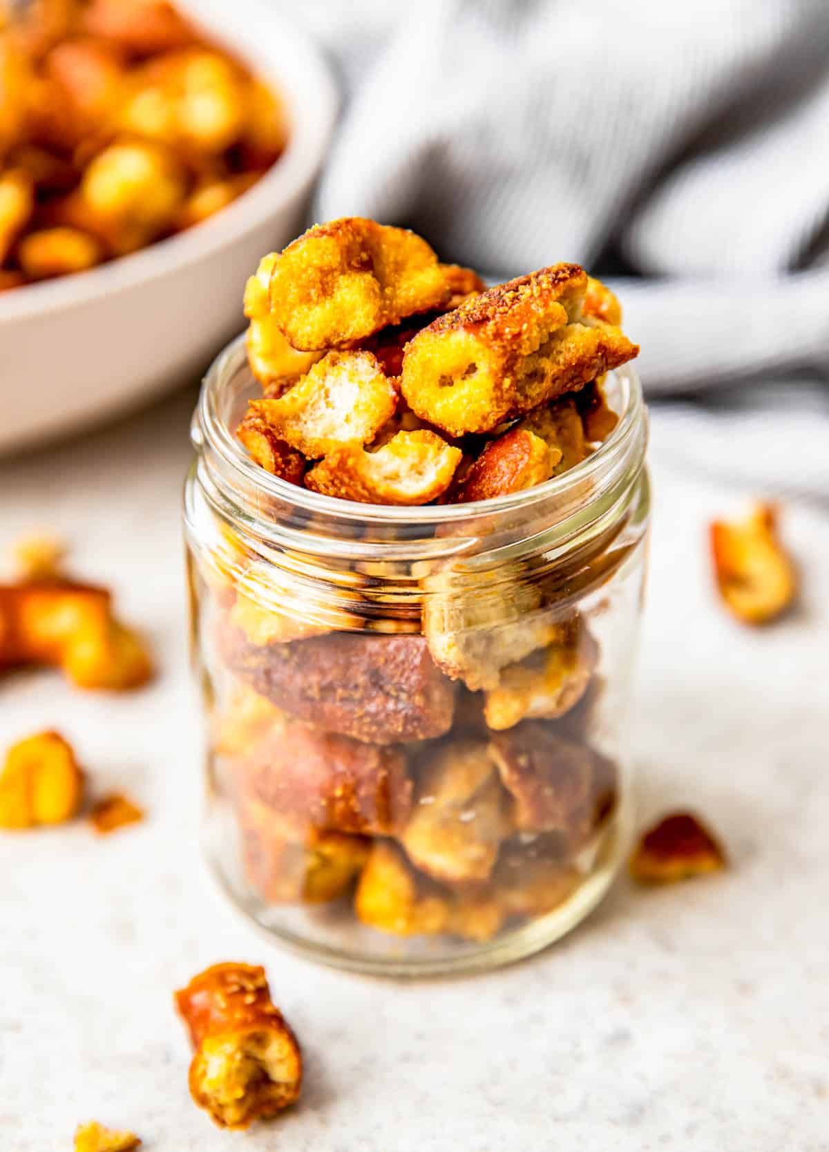 A small glass jar is filled with honey mustard pretzels. 