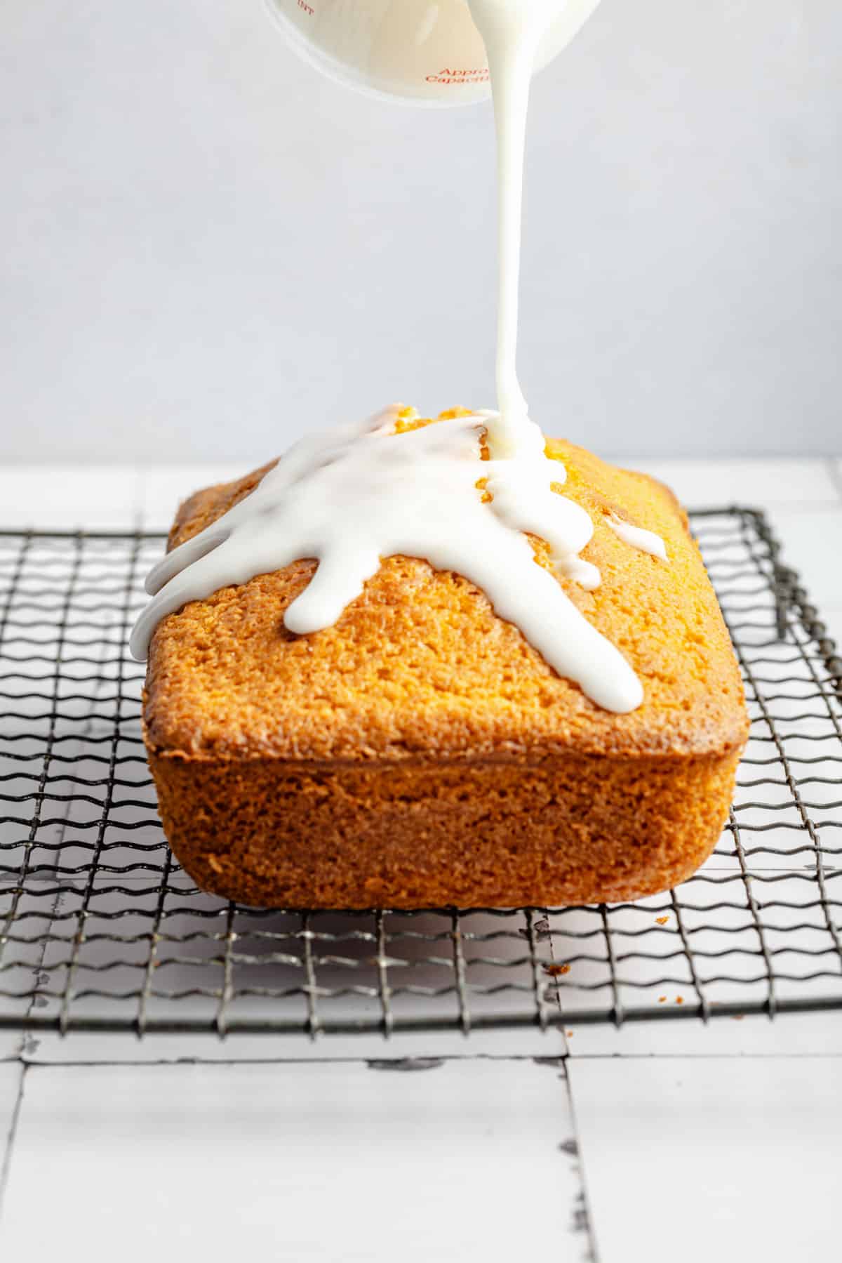 Icing is being drizzled on top of lemon pound cake.