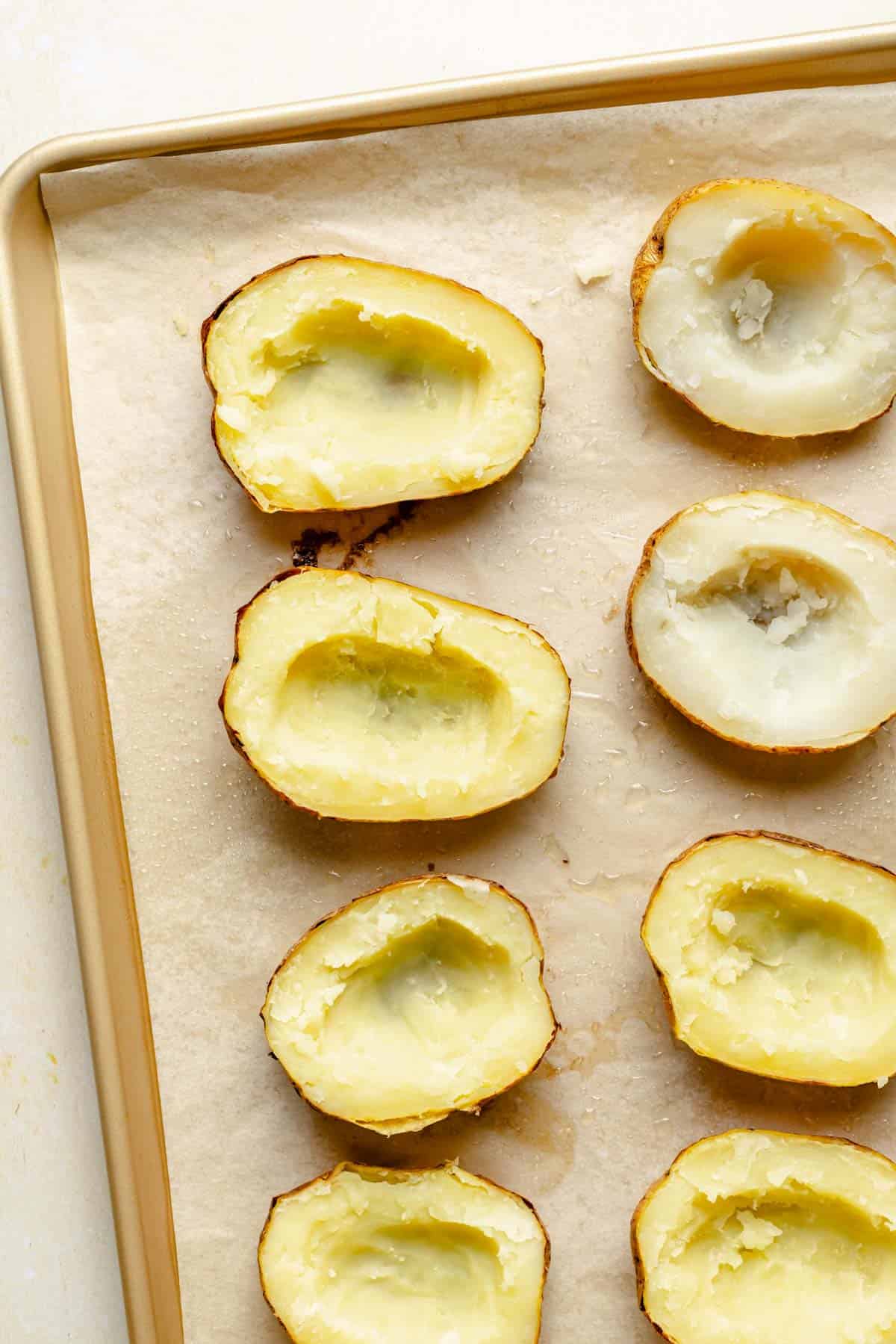 baked potatoes have had their middles scooped on a baking sheet