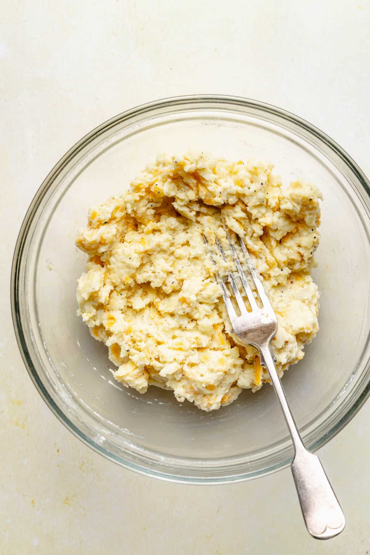 a fork is mashing together the potato filling in a glass bowl