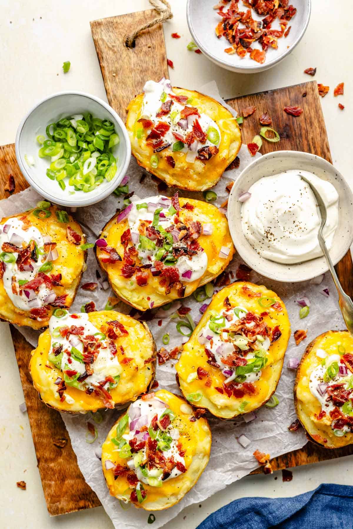 bacon, green onions and sour cream are presented in small dishes next to twice baked potatoes