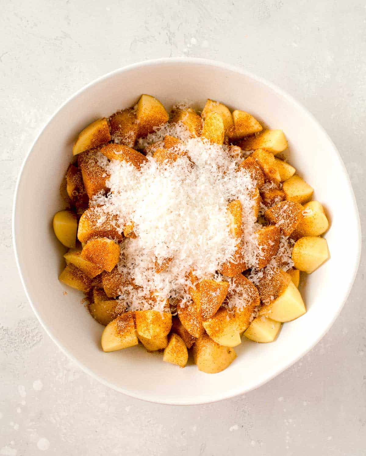 seasonings and freshly grated parmesan cheese on top of potatoes in a white bowl