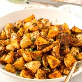 roasted parmesan potatoes in a large white bowl with gold metal spoon